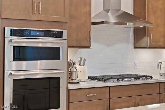 kitchen with decorative backsplash, light countertops, wall chimney exhaust hood, and appliances with stainless steel finishes