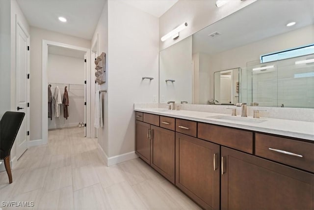 bathroom featuring double vanity, a spacious closet, a stall shower, and a sink