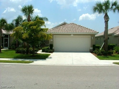 view of front of house with stucco siding, a front yard, a garage, driveway, and a tiled roof