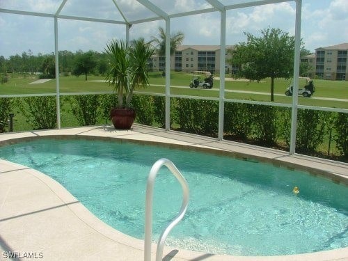 outdoor pool with glass enclosure, a lawn, and a patio