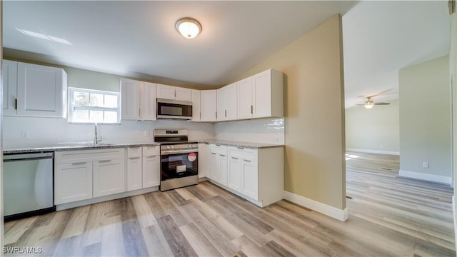 kitchen featuring white cabinets, light stone countertops, stainless steel appliances, and a sink