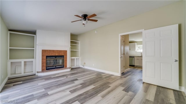 unfurnished living room with a fireplace, wood finished floors, a ceiling fan, and baseboards