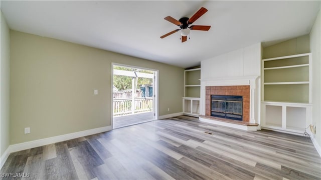 unfurnished living room with built in shelves, baseboards, a tiled fireplace, and wood finished floors