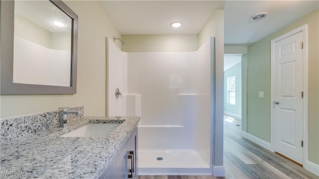 full bath featuring a shower, visible vents, vanity, wood finished floors, and baseboards