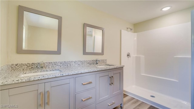 bathroom with wood finished floors, a shower, double vanity, and a sink