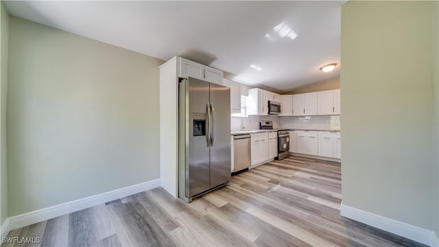 kitchen featuring stainless steel appliances, light countertops, backsplash, white cabinets, and vaulted ceiling