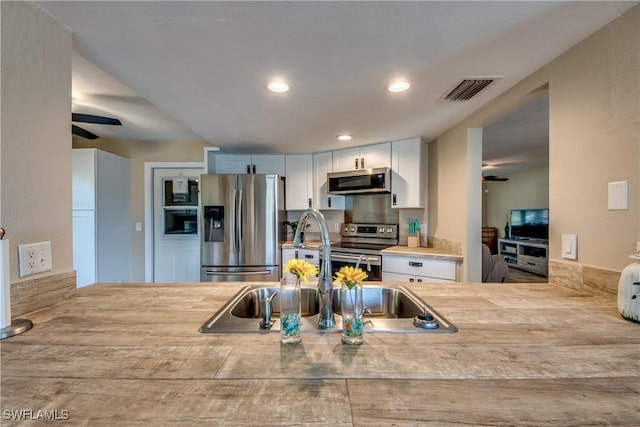 kitchen with stainless steel appliances, light countertops, visible vents, white cabinetry, and a sink