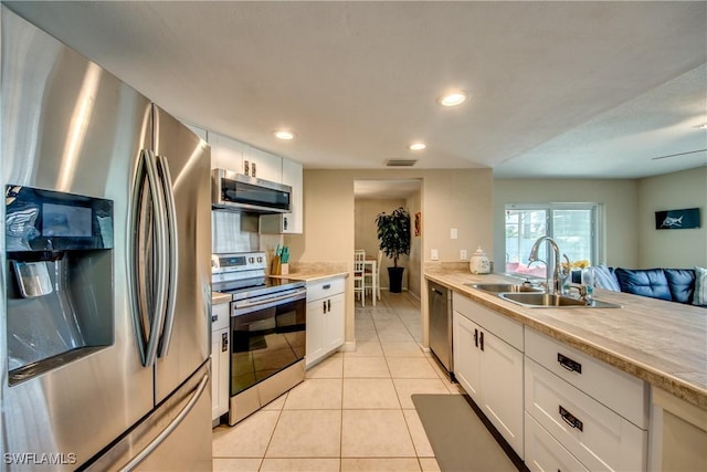 kitchen with light tile patterned floors, light countertops, appliances with stainless steel finishes, white cabinets, and a sink