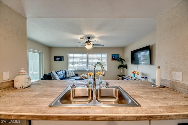 kitchen featuring visible vents, a ceiling fan, open floor plan, light countertops, and a sink