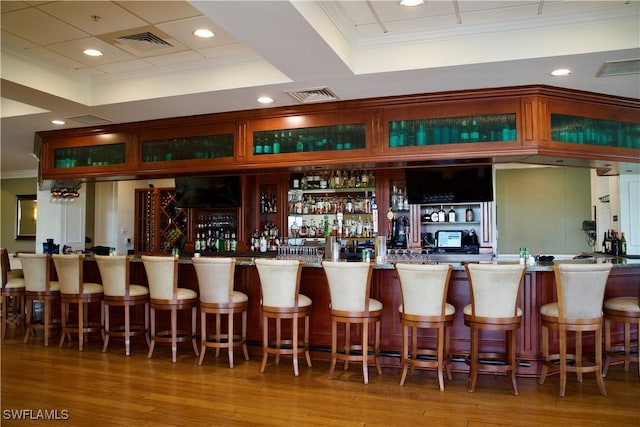 bar with wet bar, visible vents, crown molding, and wood finished floors