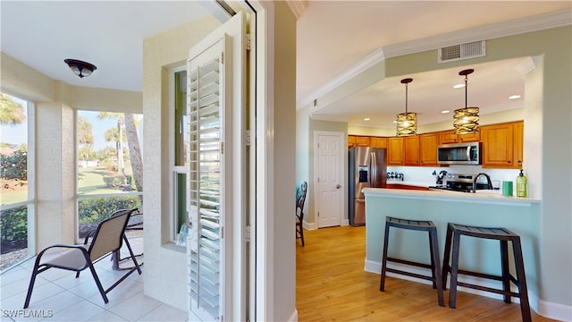 kitchen with visible vents, brown cabinetry, appliances with stainless steel finishes, ornamental molding, and a peninsula