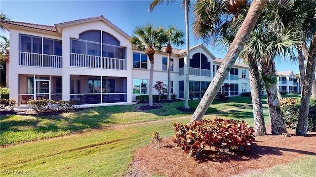 back of property with a sunroom, a yard, and stucco siding