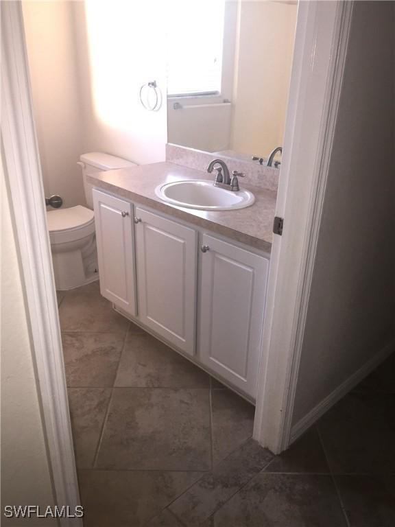 half bathroom with toilet, tile patterned flooring, and vanity