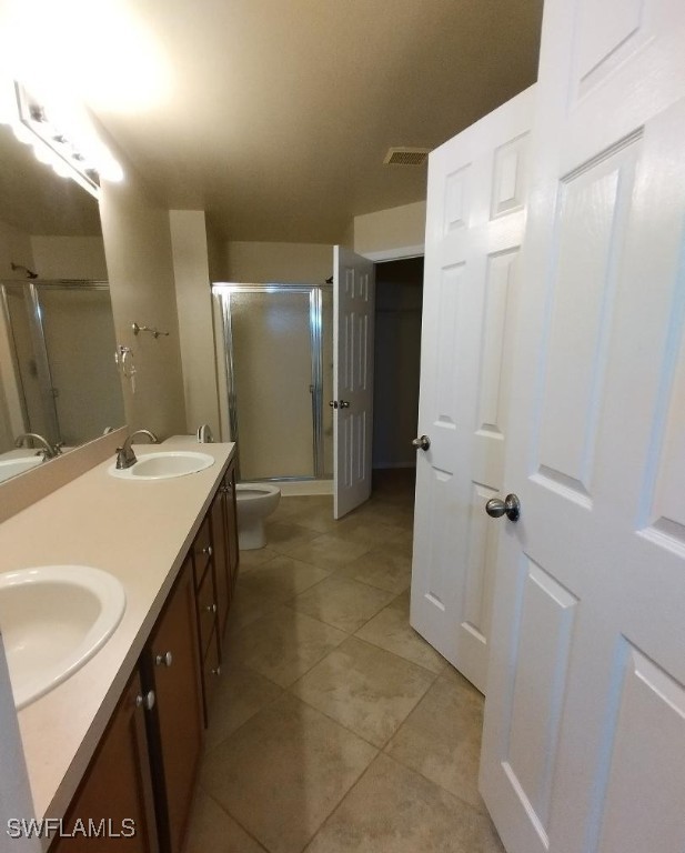 full bath featuring a stall shower, a sink, toilet, and double vanity