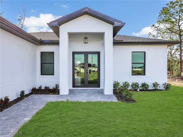 property entrance featuring stucco siding, french doors, a yard, and roof with shingles