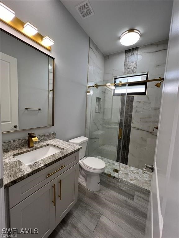 bathroom with a marble finish shower, toilet, visible vents, wood finished floors, and vanity