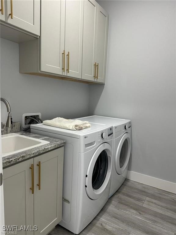 clothes washing area featuring washer and clothes dryer, a sink, light wood-style floors, cabinet space, and baseboards