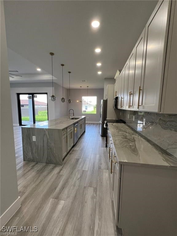 kitchen featuring a large island, stainless steel appliances, light wood-style flooring, decorative backsplash, and a sink