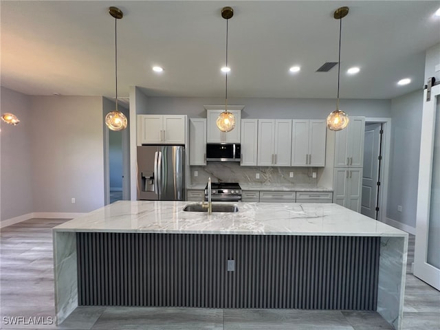 1104 Alaska Ave, Lehigh Acres, FL 33971 - kitchen featuring stainless steel appliances, decorative backsplash, a large island with sink, white cabinets, and decorative light fixtures