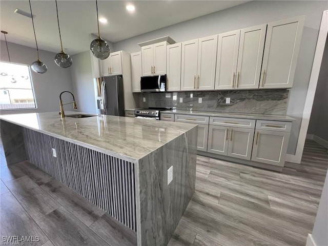 kitchen featuring appliances with stainless steel finishes, a large island with sink, a sink, and tasteful backsplash