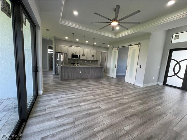 kitchen with a barn door, a center island with sink, appliances with stainless steel finishes, open floor plan, and a tray ceiling