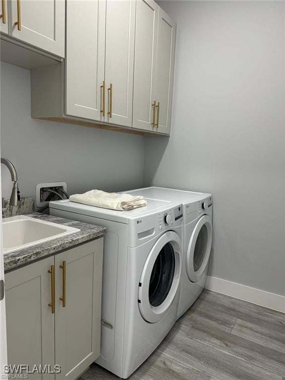 washroom featuring cabinet space, baseboards, light wood-style flooring, washer and dryer, and a sink