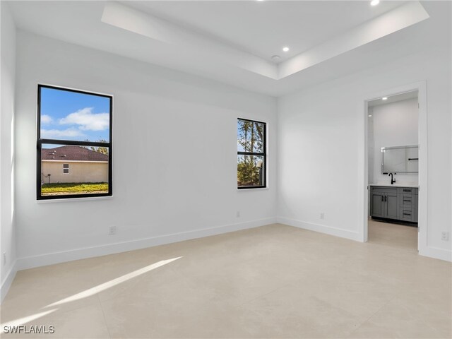 empty room with recessed lighting, a raised ceiling, and baseboards