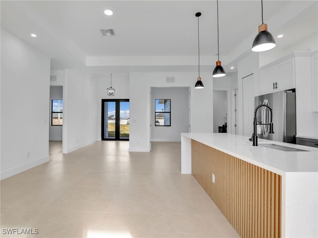 kitchen featuring recessed lighting, light countertops, visible vents, freestanding refrigerator, and an island with sink