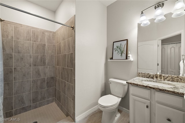 bathroom with toilet, baseboards, tiled shower, and vanity