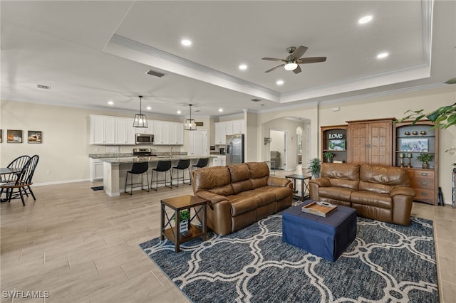 living room featuring ornamental molding, a tray ceiling, visible vents, and arched walkways