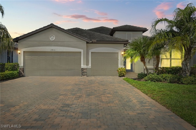 mediterranean / spanish house featuring a garage, stone siding, decorative driveway, and stucco siding