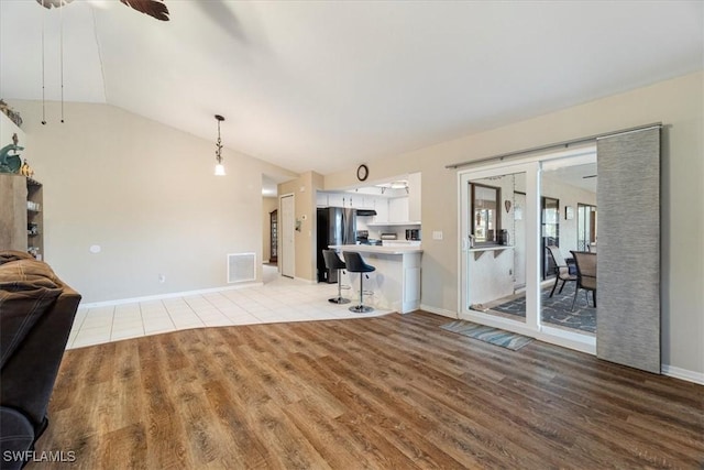 living room with visible vents, light wood-style floors, a ceiling fan, vaulted ceiling, and baseboards