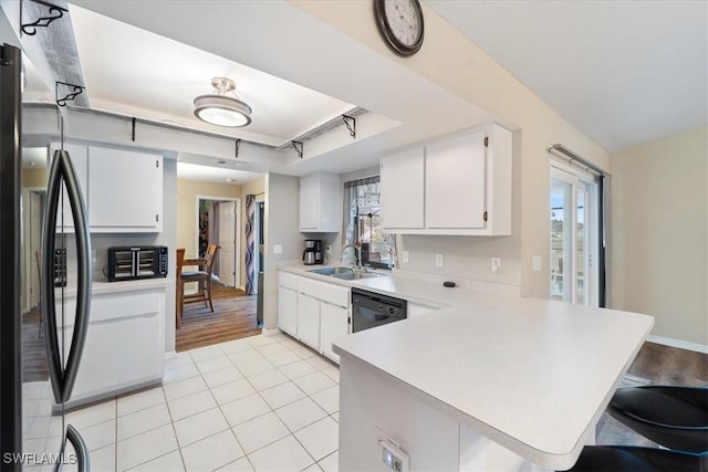 kitchen featuring a breakfast bar area, a peninsula, a sink, light countertops, and black appliances