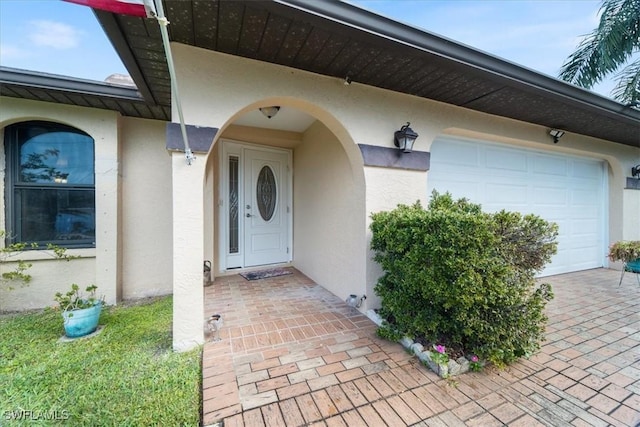 view of exterior entry with an attached garage and stucco siding