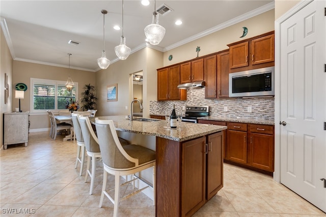 kitchen featuring visible vents, under cabinet range hood, appliances with stainless steel finishes, brown cabinetry, and a sink