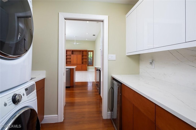 laundry room with baseboards, dark wood finished floors, cabinet space, stacked washer and dryer, and wine cooler