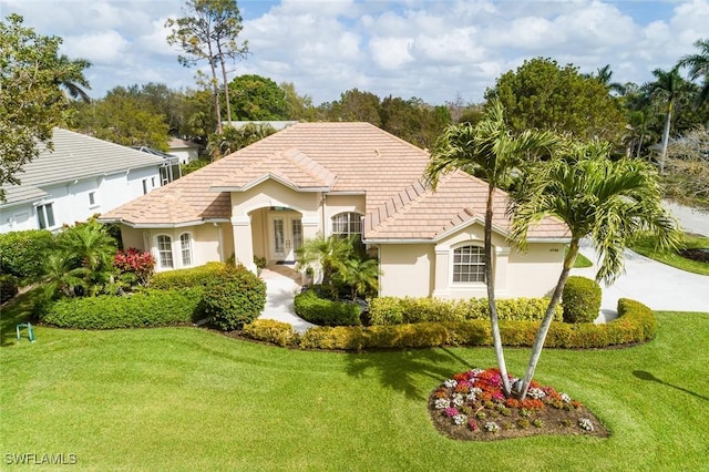 mediterranean / spanish home with a tile roof, stucco siding, concrete driveway, and a front lawn