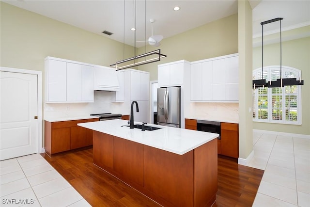 kitchen with modern cabinets, a sink, stainless steel fridge, light countertops, and a towering ceiling