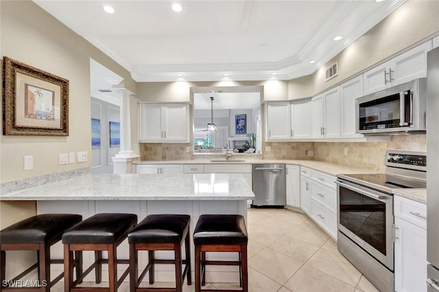 11596 Quail Village Way, Naples, FL 34119 - kitchen with appliances with stainless steel finishes, decorative columns, a sink, a peninsula, and a kitchen bar