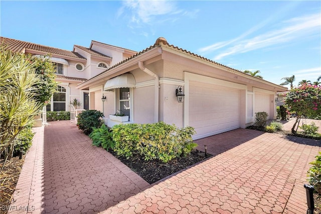 11596 Quail Village Way, Naples, FL 34119 - view of front facade with stucco siding, an attached garage, decorative driveway, and a tiled roof