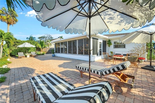 view of patio / terrace featuring a sunroom, fence, and outdoor dining space