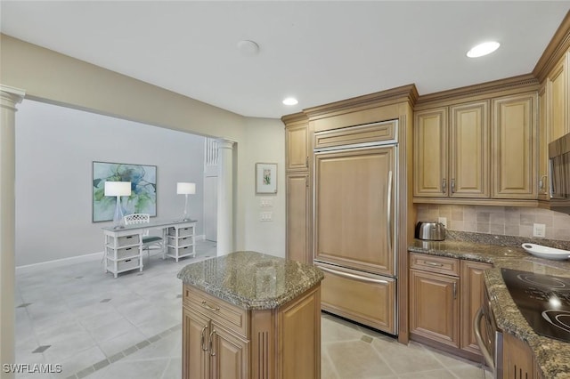 kitchen with black electric stovetop, tasteful backsplash, dark stone countertops, paneled built in refrigerator, and ornate columns