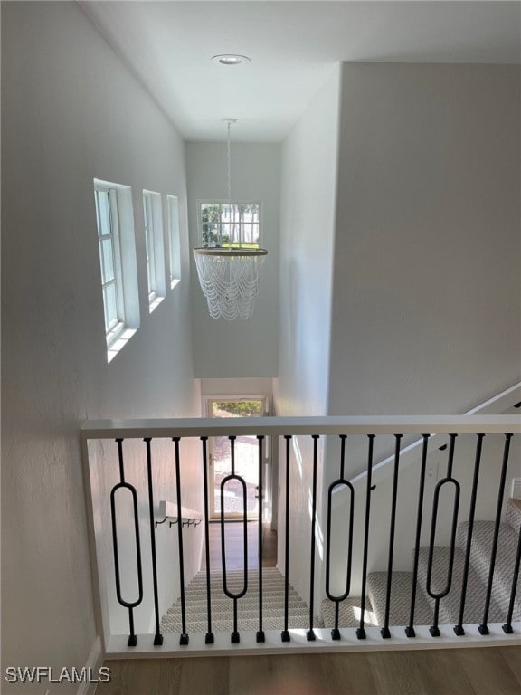 stairs with wood finished floors and an inviting chandelier