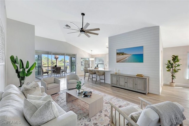 living room with a ceiling fan, baseboards, visible vents, light wood finished floors, and high vaulted ceiling