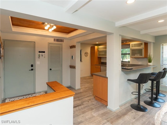 kitchen with visible vents, light wood-type flooring, a tray ceiling, beamed ceiling, and a kitchen bar