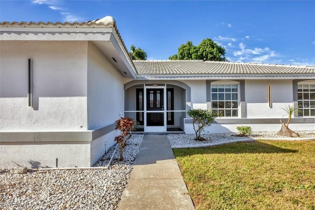 view of exterior entry featuring a lawn, a tile roof, and stucco siding