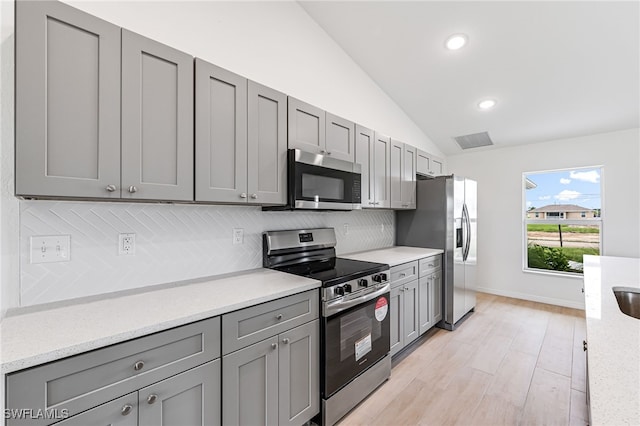 kitchen with lofted ceiling, appliances with stainless steel finishes, gray cabinets, and backsplash