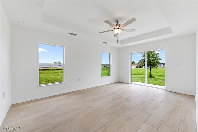 empty room featuring a tray ceiling, visible vents, light wood-style flooring, a ceiling fan, and baseboards