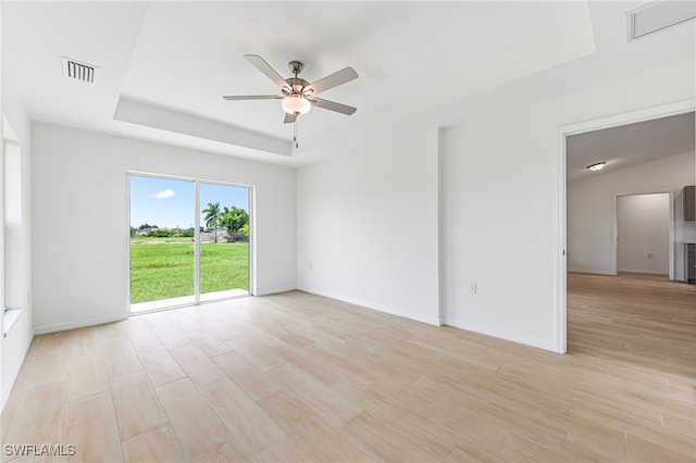 empty room with ceiling fan, visible vents, baseboards, light wood-type flooring, and a tray ceiling