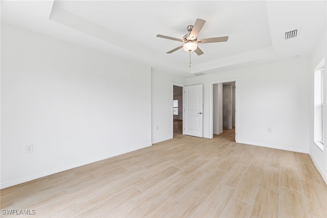 unfurnished bedroom with light wood finished floors, visible vents, baseboards, a raised ceiling, and a ceiling fan